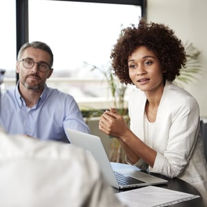 two people sit in a meeting with a laptop open
