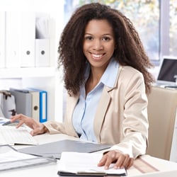 Portrait of beautiful smiling afro-american office worker sitting at desk, using computer