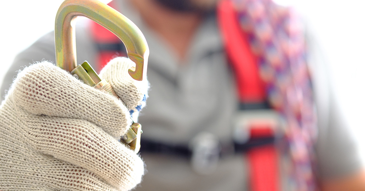image of a gloved hand with a safety clip with blurred person in background in safety harness