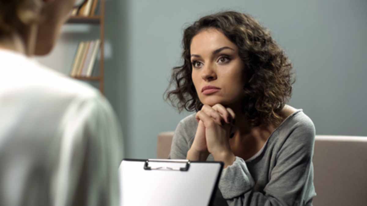 woman sitting in a chair and listening to another person who is holding a clipboard 