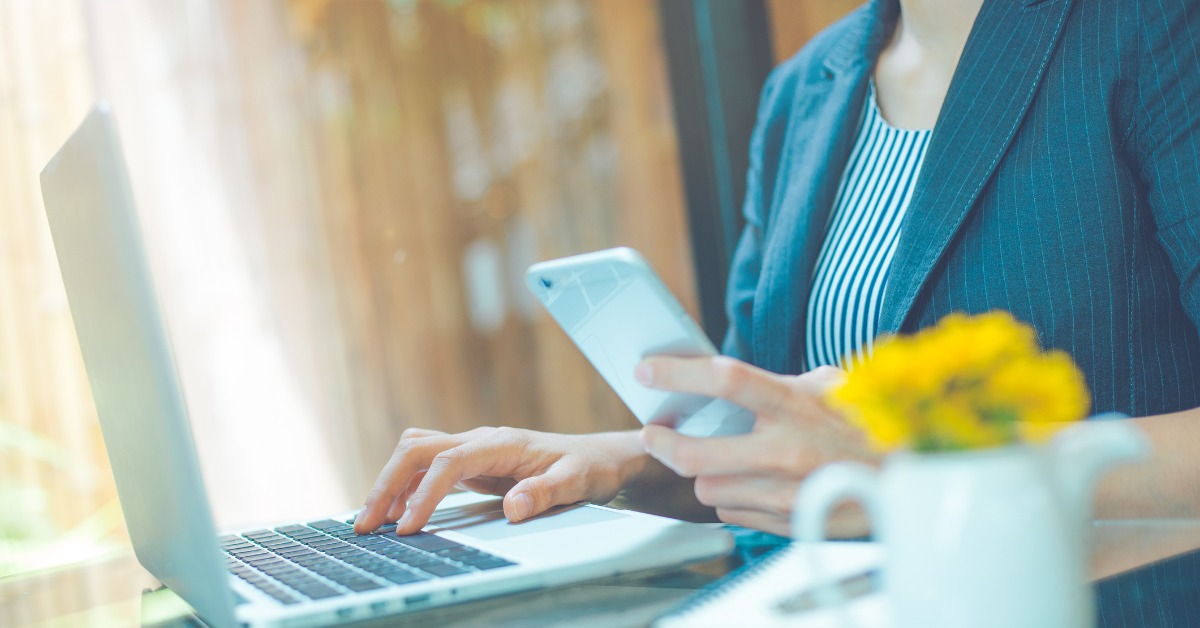 woman working on laptop holding her phone with a yellow flower on the desk