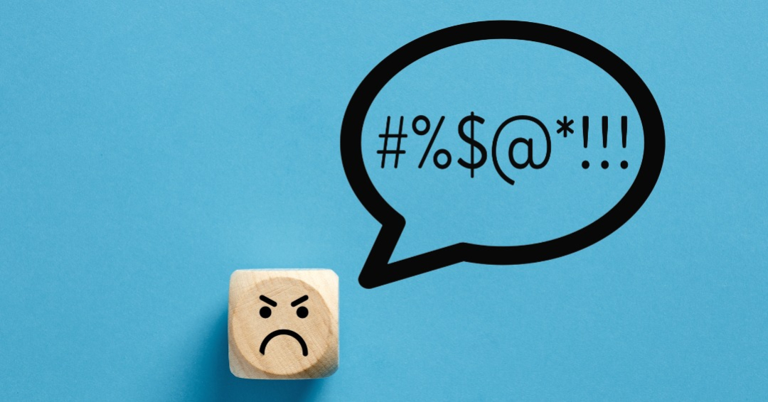 Angry face icon on a wooden cube with swearing or swearwords icons in a speech bubble. Swearing and bad language concept