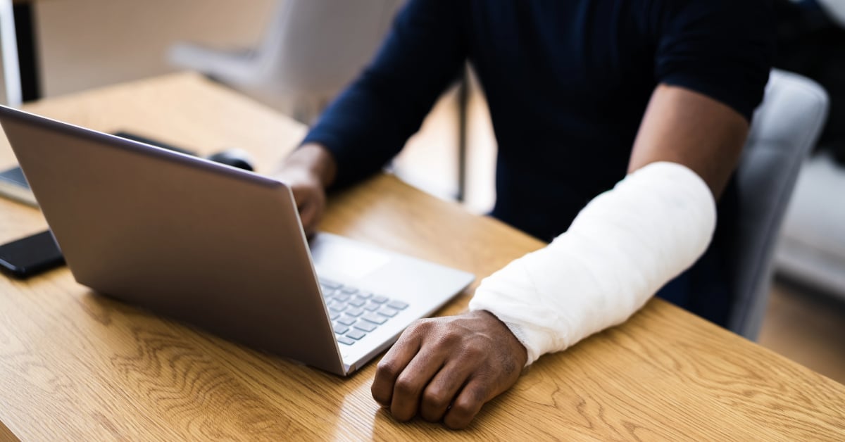 Injured Worker Compensation. Broken Arm African Man On Computer