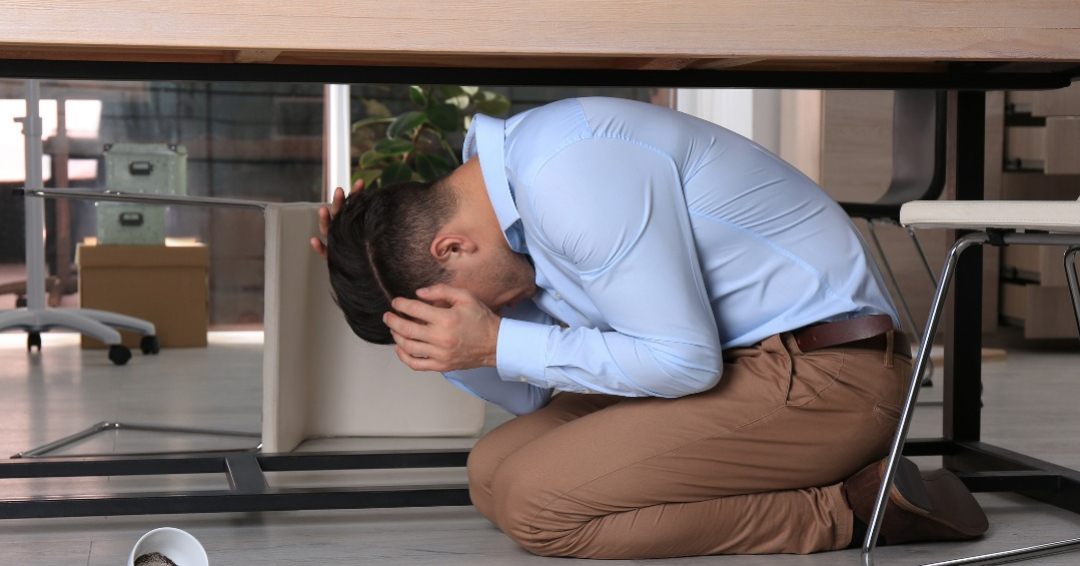 man hiding under desk during earthquake