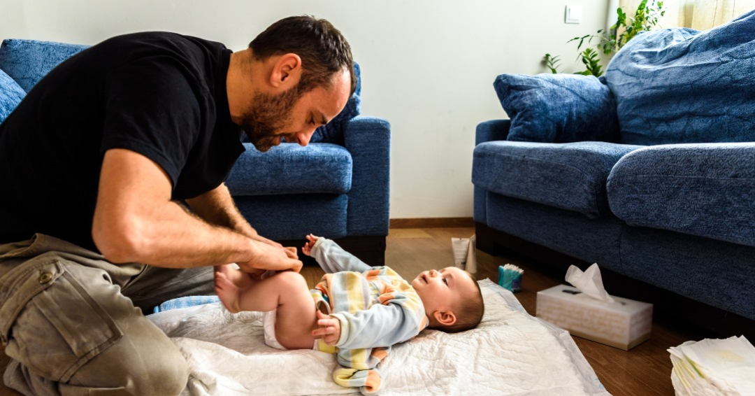 father changing baby's diaper on a blanket on the floor