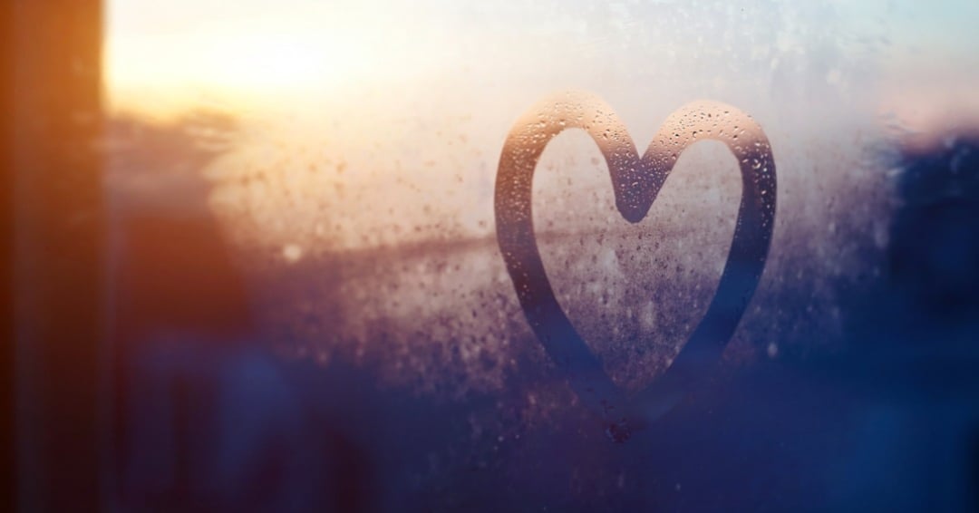 image of a heart drawn on a window with a sunrise in the background