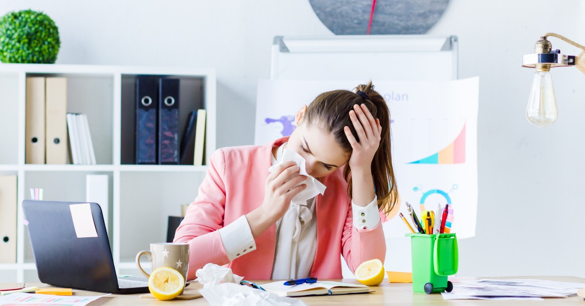 Woman sitting at office desk with tissues and cup of tea with lemon