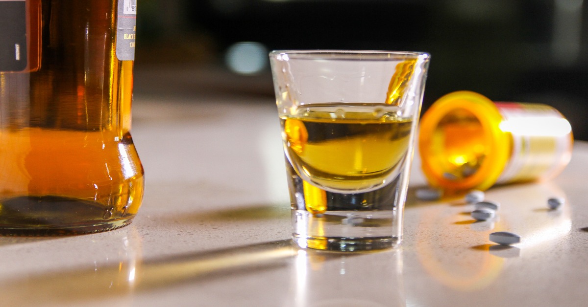 glass of alcohol and a bottle of pills on a table