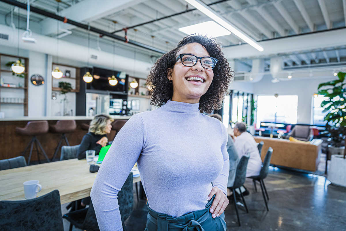 GettyImages-1296597122-Portrait of a beautiful, young woman wearing glasses standing at a big modern office
