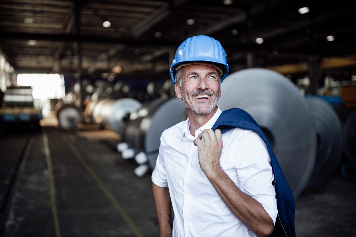 GettyImages-1338886140-Cheerful male engineer with hardhat holding blazer at warehouse