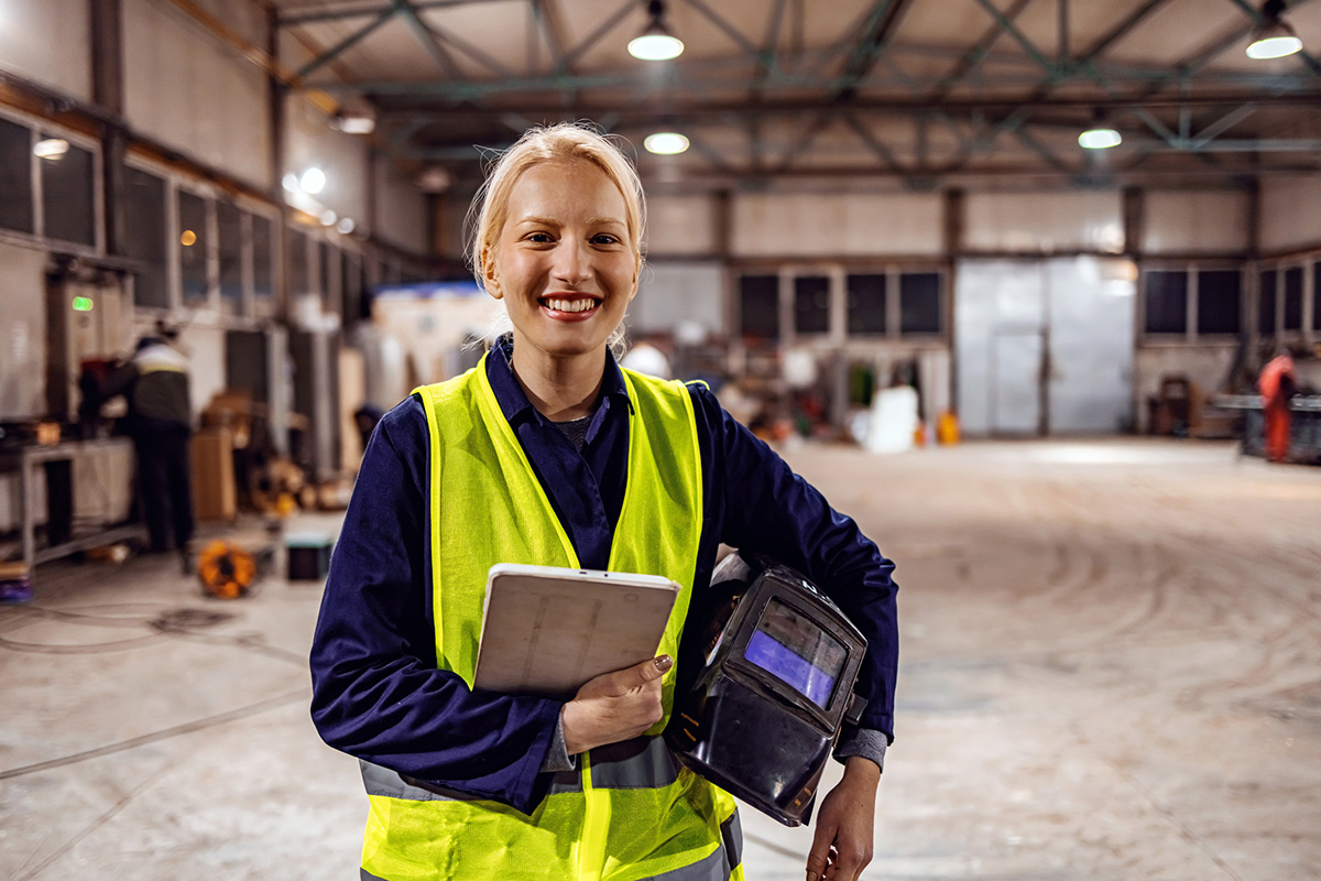 GettyImages-1358926120-Smiling Successful Female Industrial Specialist Walking in a Metal Manufacture Warehouse, looking at camera.