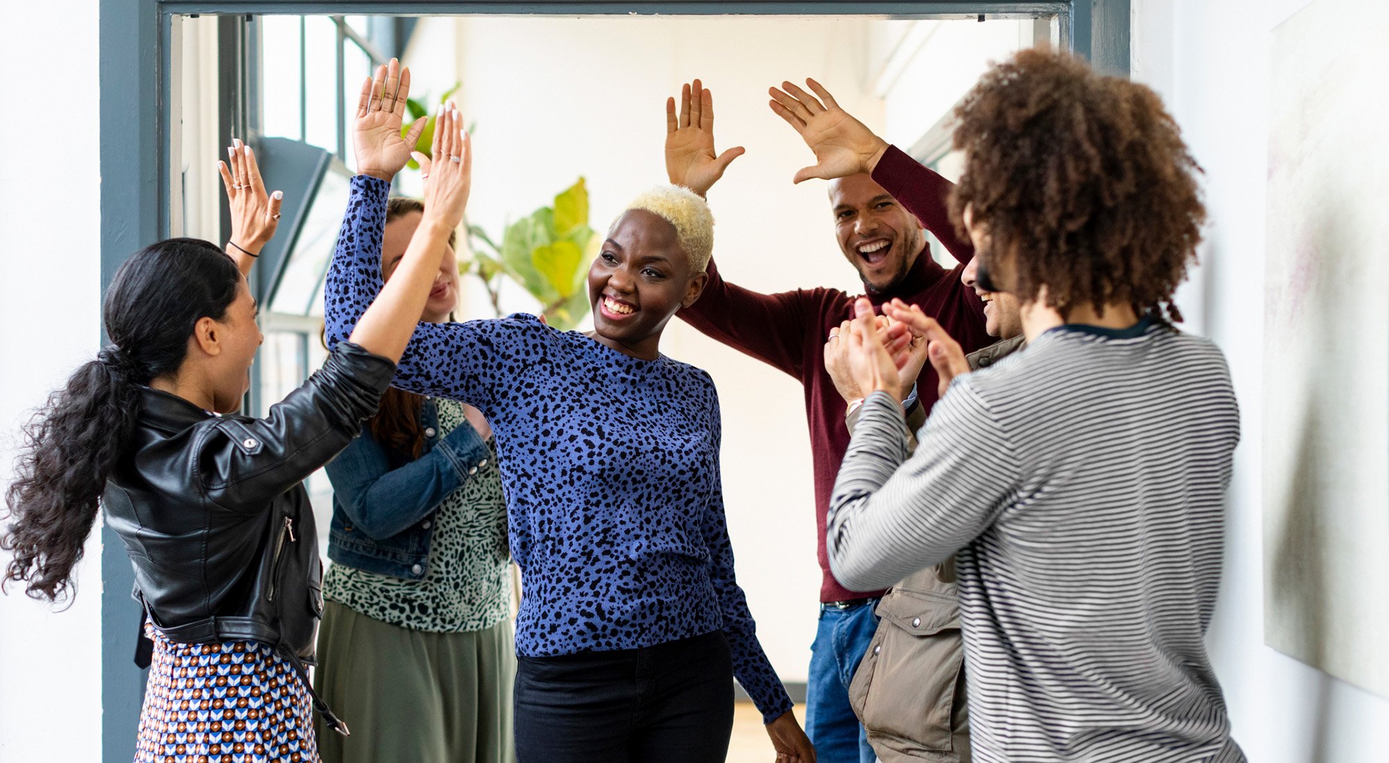 GettyImages-1396315205-Six smiling business colleagues high fiving and cheering in office