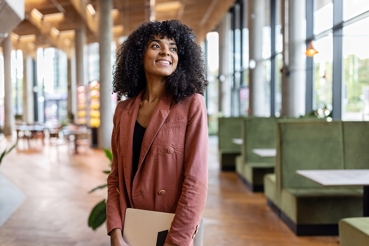 GettyImages-1450789013-Portrait of a young woman standing in office cafe looking away. Businesswoman at creative office.