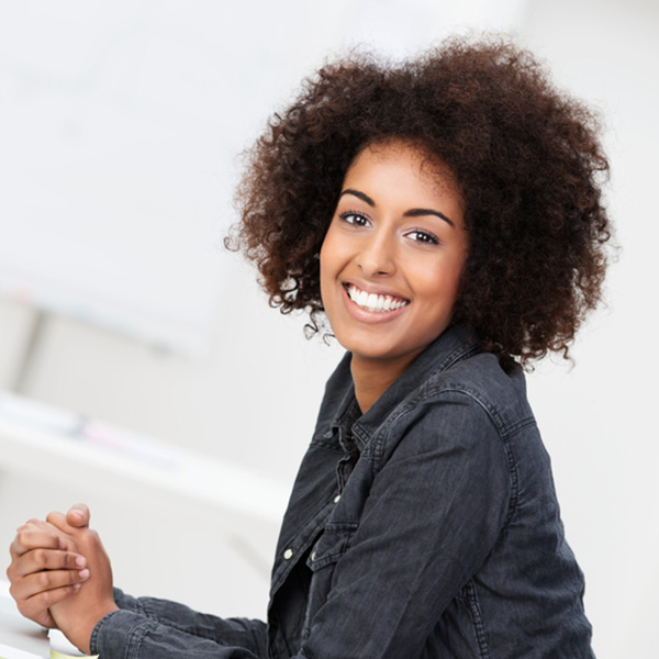 Happy contented young African American woman with an afro hairstyle sitting at her desk in front of a laptop