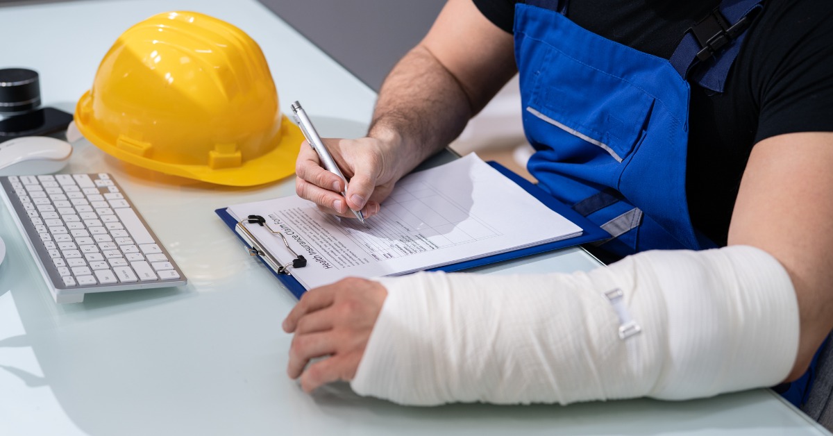 worker at desk with left arm in cast, right hand working on paperwork 